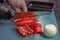 Cook cuts red pepper with a kitchen knife in a street cafe.