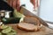 Cook cutting baked meat on board with sharp kitchen knife and fork closeup