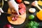 Cook cutting meat on a wooden board and fresh raw vegetables on dark table.