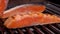 Cook flips a raw salmon with metal tongs on grill