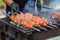 The cook fries juicy steaming meat on a charcoal grill. Food and cooking equipment at a street food festival