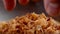 Cook hand takes fried onion flakes from a wooden bowl.