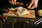 The cook prepares a chicken leg on a kitchen board with spices. Spoon in chef hand to add allspice to chicken thigh for flavor