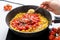 The cook puts the garlic in the Pan with Chopped Bell Peppers, Tomatoes and Onions, which are fried on the Stove. Recipe and