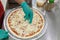 Cook`s hand with green gloves putting cheese on raw pizza.