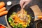 Cook`s hands stir hot vegetables and meat in a wok. Top view, close-up