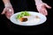 The cook serves a prepared fish dish. Salmon in creamy caviar sauce on a white plate. Lettuce leaves. Photo on a black background