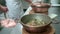 A cook showing clams in copper pot covered with lid