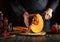 The cook uses a knife to cut a ripe pumpkin into slices on a wooden board. The concept of preparing a pumpkin dish with viburnum