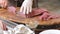 Cook in white gloves cuts off small pieces of steaks from a large piece of raw meat. Quality pork tenderloin for the