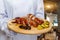 A cook with a wooden tray with pork shank on it