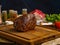 Cooked appetizing meat ham on a wooden cutting board. In the background is a piece of raw meat, spices, herbs, salt on a dark blue