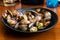 Cooked clams on black ceramic plate on wooden table of restauran
