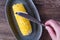 Cooked corn on the cob on a gray dish, womanâ€™s hand with knife spreading butter