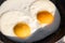 Cooked fried eggs with two bright round raw yolks in a black skillet in sun light. Simple breakfast option. Top view, close-up