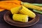 Cooked and raw corncobs on a dark wooden background