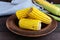 Cooked and raw corncobs on a dark wooden background