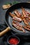 Cooked sizzling hot tasty crispy bacon on a skillet. Farm organic meat. Black background. Top view