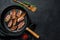 Cooked sizzling hot tasty crispy bacon  on a skillet. Farm organic meat. Black background. Top view. Space for text