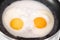 Cooked small fried eggs with two bright round raw yolks in a black skillet. Simple breakfast. Top view, close-up