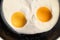Cooked tender, soft fried eggs with two bright round raw yolks in whites a in black frying pan. Simple breakfast in light of sun