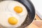 Cooked tender, soft fried eggs with two bright round raw yolks in whites with edge cracks a in black dark frying pan. Simple break