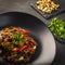 Cooked vegetables on black plate and dark background, garlic, red pepper, green onion.
