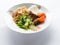 Cooked white rice, fried noodles on a white plate, topped with sliced green vegetables plus tomatoes and sliced fried tempeh