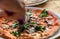 Cooker cutting hot pizza in restaurant. Tasty pizza with with cheese and greens, closeup view. Popular italian food