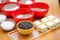 Cookery set of colorful bowls with chocolate drops, flour, cocoa powder, sugar and blocks of butter stand at light brown wooden ta