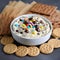 Cookie dough dip in a bowl with chocolate chips and colorful candy alongside biscuits, close-up dessert shot