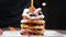 Cooking art. Chef spreading caramel on top of stack of fresh fluffy pancakes decorated with forest berries. Homemade