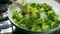 Cooking broccoli and green beans in a frying pan. Stirring with a wooden spoon.