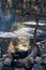 Cooking at campfire. Black charred pot at bonfire with clouds of smoke in sunset lights. Trekking or hiking cuisine