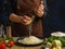 Cooking dishes from cheese, vegetables, herbs. Professional chef grates cheese on a wooden kitchen table, dark blue background.