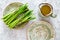 Cooking fresh asparagus. Greens on plate near a jug of oil on grey stone background top view