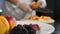 Cooking fresh salad and flambe fruit. Blurred image of chef hands slicing juicy apricot shot through berries on plate