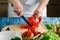 cooking and home concept - close up of female hand cutting tomato on cutting board with sharp knife