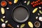 Cooking mockup. Frying pan among spices and vegetables on black desk top-down copy space