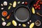 Cooking mockup. Frying pan among spices and vegetables on black desk top-down copy space