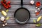 Cooking mockup. Frying pan among spices and vegetables on dark wooden desk top-down copy space