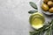 Cooking oil in bowl, olives and rosemary on light gray textured table, flat lay. Space for text