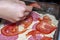 Cooking pizza. Hand lays slices of tomatoes on the dough. Close-up