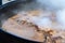 Cooking real Uzbek pilaf. Stewing lamb ribs in a huge cauldron with lots of steam outside during a traditional folk festival