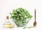 Cooking setting with green spinach leaves in glass bowl, olive oil and wooden spoon at white background. Healthy food preparation