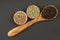 A cooking spoon made of olive wood with black peppercorns and two wooden bowls filled with green and white peppercorns