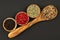 A cooking spoon made of olive wood with white peppercorns and three wooden bowls filled with green, red and black peppercorns
