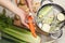 Cooking tasty bouillon. Woman peeling carrot at white wooden table, top view