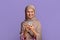 Cool application. Excited young muslim woman in hijab using smartphone, texting or browsing internet, purple background