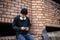 A cool Asian man with his skateboard is sitting at an unknown abandoned building, using his phone